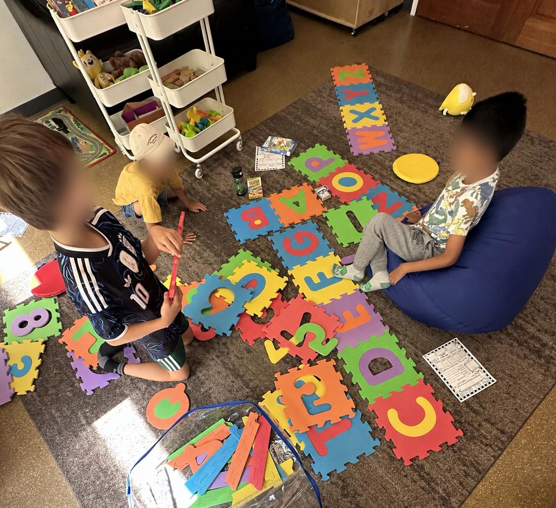 Children exploring foam letters and numbers laid out on the floor. Faces are blurred.