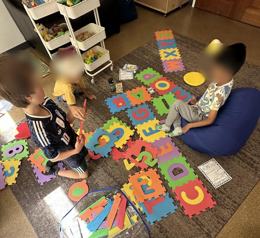 Children matching letters and numbers on a foam floor puzzle together. Faces are blurred.
